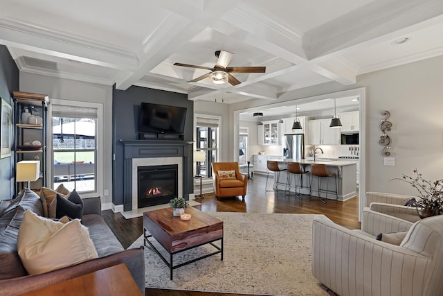 living room featuring beam ceiling, dark wood-type flooring, ceiling fan, crown molding, and coffered ceiling