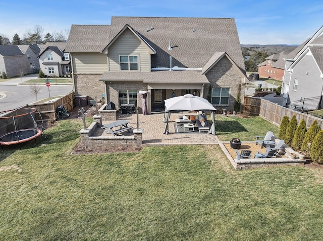 back of house featuring a fire pit, a trampoline, a patio area, a gazebo, and a yard