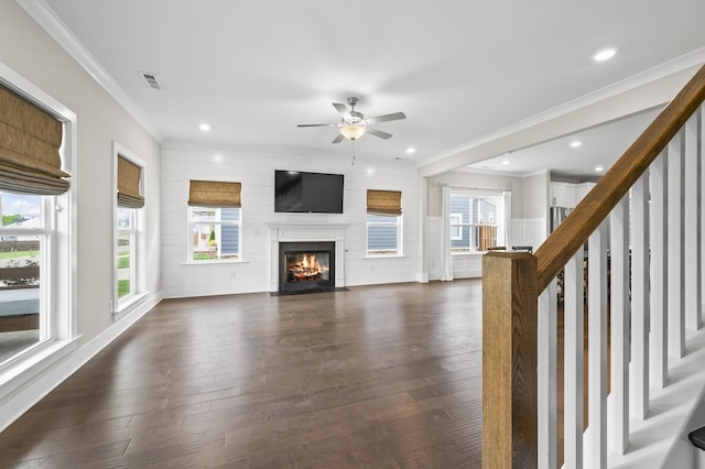 unfurnished living room featuring ceiling fan, dark hardwood / wood-style flooring, crown molding, and a healthy amount of sunlight