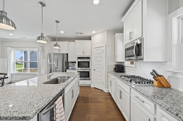 kitchen with sink, pendant lighting, stainless steel appliances, and an island with sink