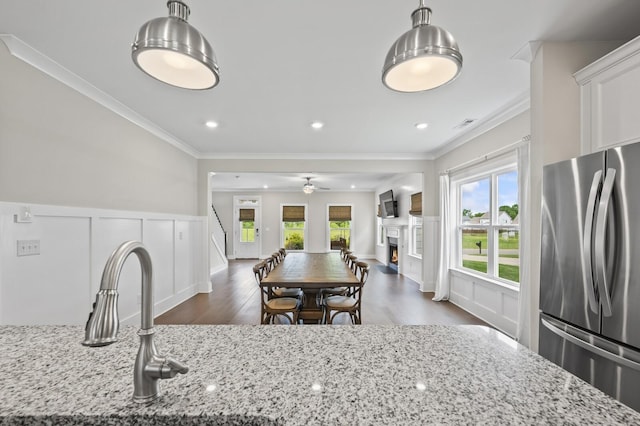 kitchen with light stone countertops, decorative light fixtures, crown molding, and stainless steel refrigerator