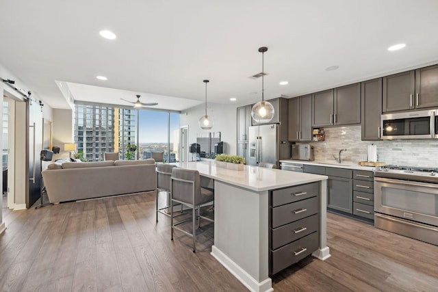 kitchen featuring appliances with stainless steel finishes, a kitchen island, a barn door, hanging light fixtures, and a breakfast bar area