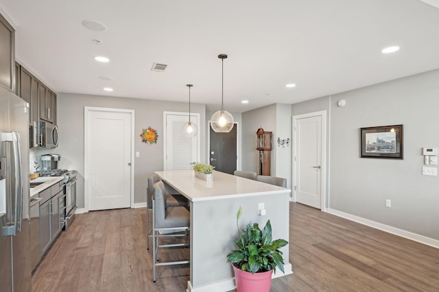 kitchen with appliances with stainless steel finishes, light wood-type flooring, hanging light fixtures, a breakfast bar, and a center island