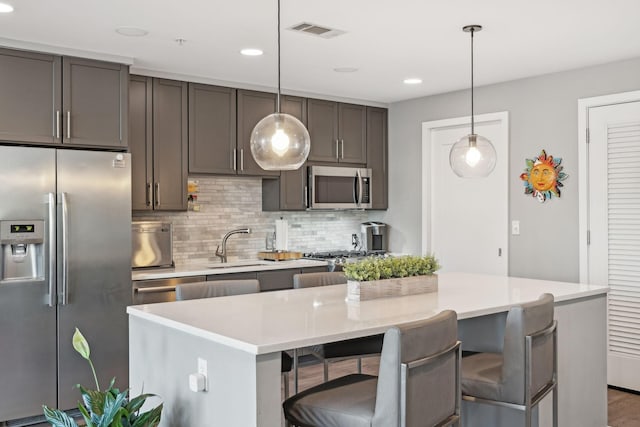 kitchen with a breakfast bar area, stainless steel appliances, decorative backsplash, hanging light fixtures, and a center island