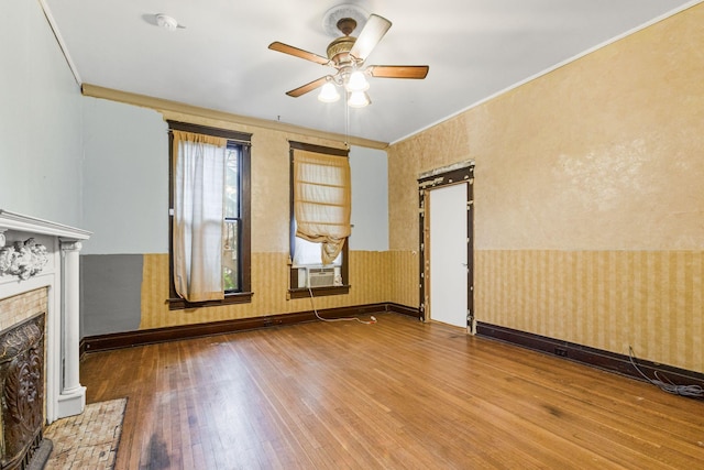 unfurnished living room with hardwood / wood-style flooring, ceiling fan, crown molding, and a tiled fireplace