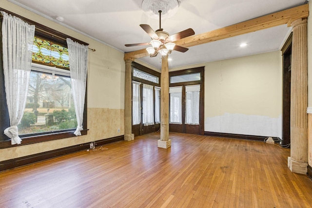 empty room featuring ceiling fan, plenty of natural light, ornate columns, and light wood-type flooring