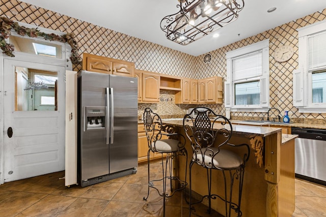 kitchen with a kitchen island, hanging light fixtures, light brown cabinets, stainless steel appliances, and light stone counters