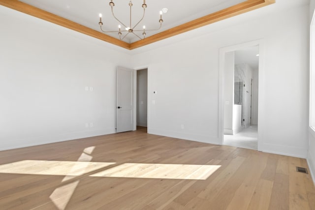 unfurnished room featuring a tray ceiling, ornamental molding, a notable chandelier, and light wood-type flooring