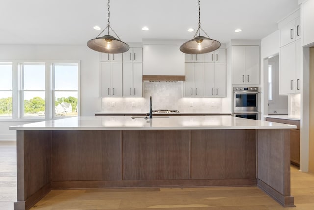 kitchen featuring pendant lighting, white cabinetry, a center island with sink, and custom exhaust hood