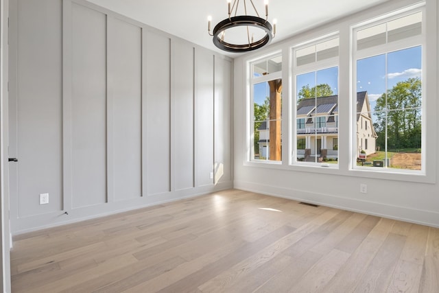 spare room featuring a notable chandelier, plenty of natural light, and light hardwood / wood-style floors