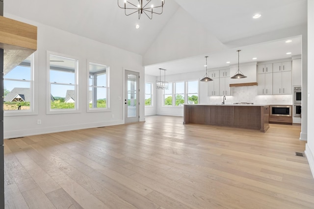 unfurnished living room featuring a chandelier, sink, light hardwood / wood-style flooring, and high vaulted ceiling