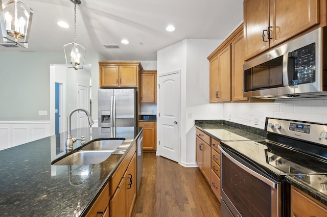 kitchen featuring pendant lighting, appliances with stainless steel finishes, dark hardwood / wood-style flooring, dark stone counters, and sink