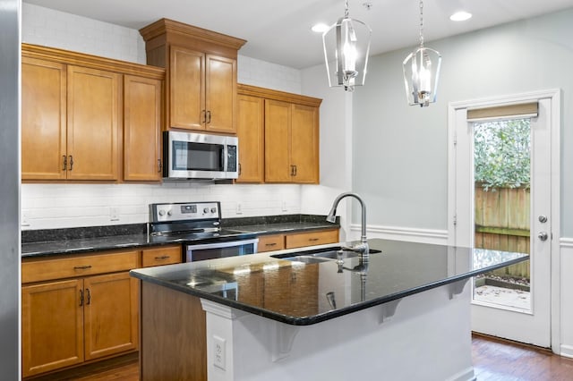 kitchen with decorative light fixtures, dark wood-type flooring, stainless steel appliances, dark stone countertops, and sink