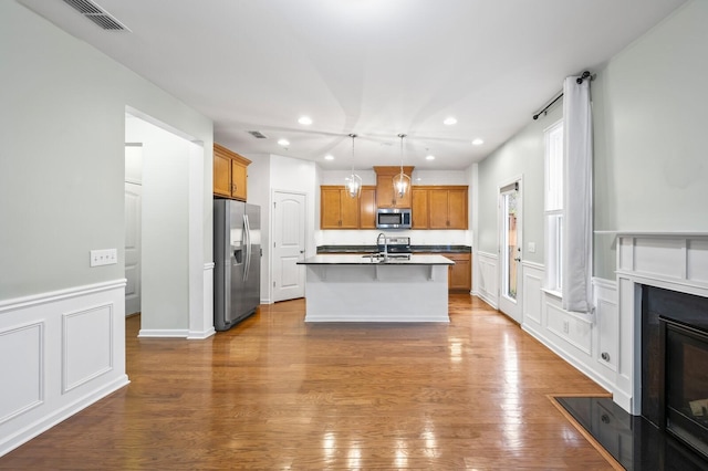 kitchen with hardwood / wood-style flooring, an island with sink, stainless steel appliances, pendant lighting, and sink