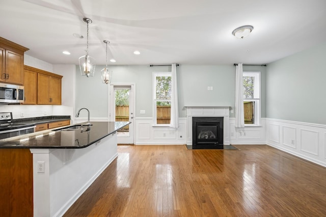 kitchen featuring appliances with stainless steel finishes, decorative light fixtures, dark stone countertops, wood-type flooring, and sink