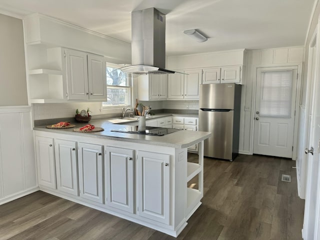 kitchen with black electric stovetop, kitchen peninsula, island exhaust hood, stainless steel refrigerator, and white cabinetry