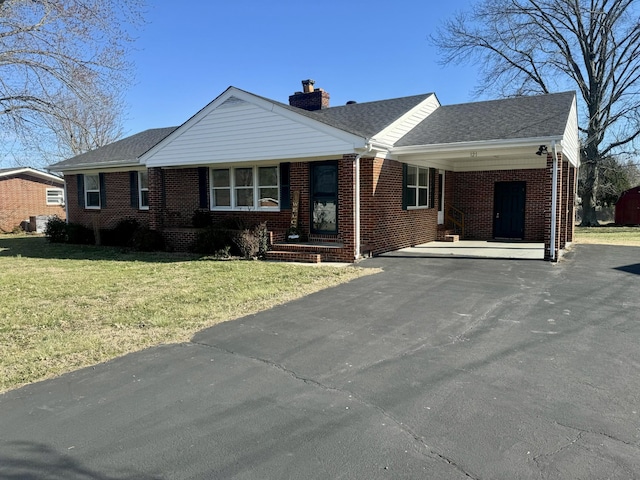 ranch-style home with aphalt driveway, brick siding, a chimney, an attached carport, and a front lawn