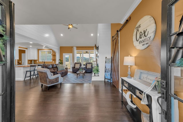 living room featuring ceiling fan, a barn door, lofted ceiling, dark wood-type flooring, and ornamental molding