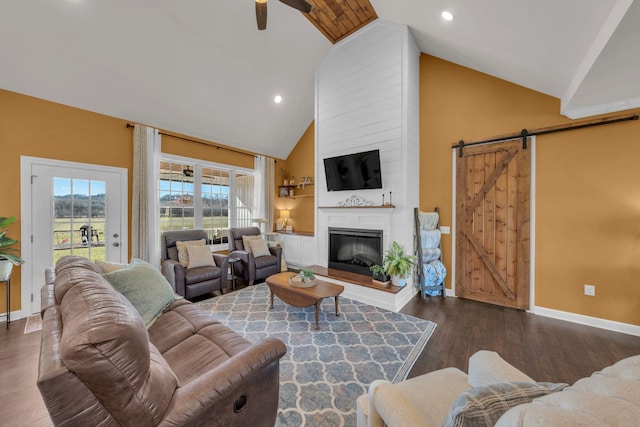 living room with ceiling fan, a barn door, dark hardwood / wood-style floors, a large fireplace, and high vaulted ceiling