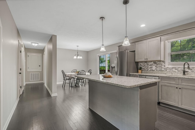 kitchen featuring decorative light fixtures, a kitchen island, stainless steel refrigerator with ice dispenser, sink, and light stone countertops