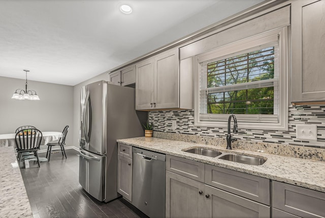 kitchen with light stone countertops, stainless steel appliances, decorative backsplash, sink, and hanging light fixtures