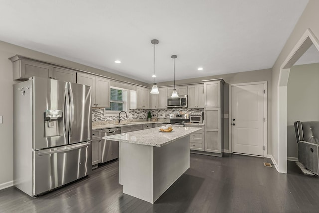 kitchen featuring a kitchen island, pendant lighting, gray cabinetry, stainless steel appliances, and light stone counters