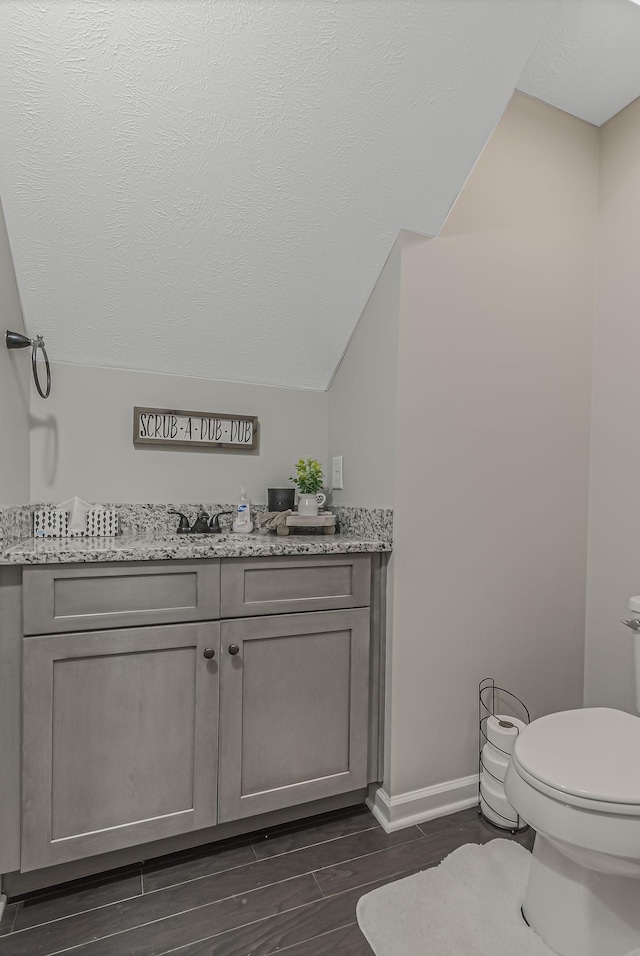 bathroom featuring wood-type flooring, toilet, vanity, and vaulted ceiling