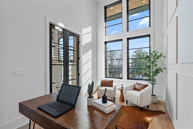 home office with a towering ceiling, hardwood / wood-style floors, and french doors