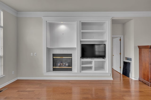 unfurnished living room featuring light wood-type flooring, crown molding, built in features, and a tile fireplace