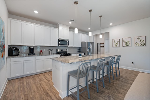 kitchen with an island with sink, appliances with stainless steel finishes, decorative light fixtures, white cabinets, and light hardwood / wood-style flooring