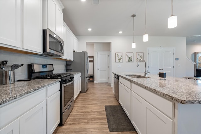 kitchen with pendant lighting, white cabinetry, stainless steel appliances, sink, and a kitchen island with sink