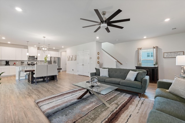 living room featuring light wood-type flooring and ceiling fan with notable chandelier