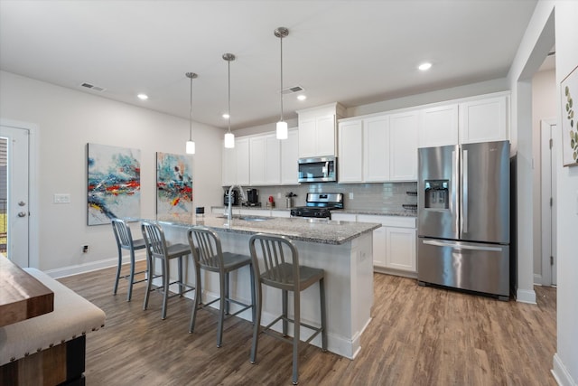 kitchen with pendant lighting, appliances with stainless steel finishes, white cabinetry, backsplash, and a center island with sink