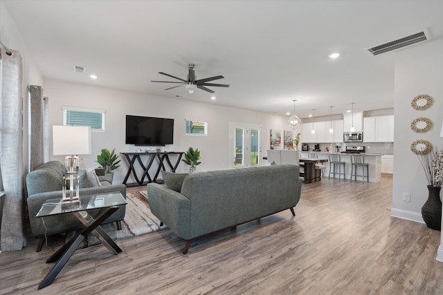 living room with ceiling fan with notable chandelier and light wood-type flooring