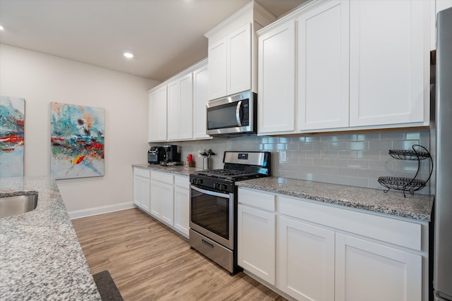 kitchen with backsplash, white cabinetry, light hardwood / wood-style flooring, appliances with stainless steel finishes, and light stone counters