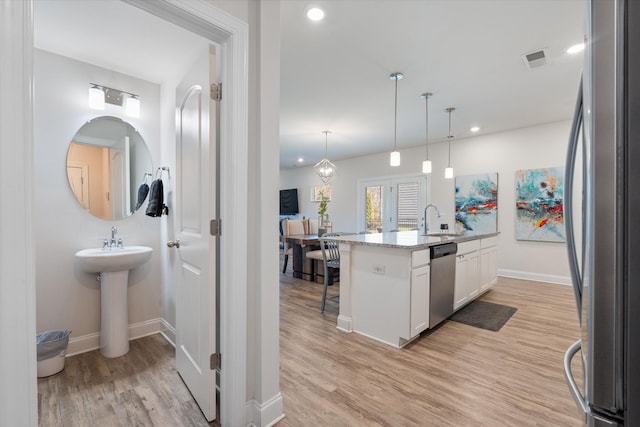 kitchen featuring decorative light fixtures, a breakfast bar, stainless steel appliances, white cabinets, and light stone counters