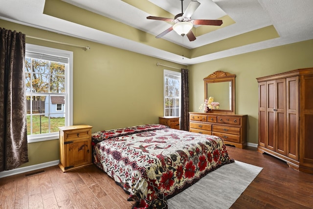 bedroom with ceiling fan, dark hardwood / wood-style flooring, and a tray ceiling