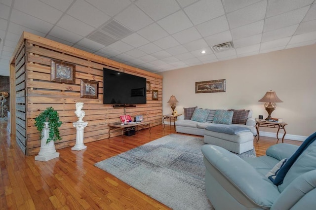 living room with hardwood / wood-style flooring, a drop ceiling, and wood walls