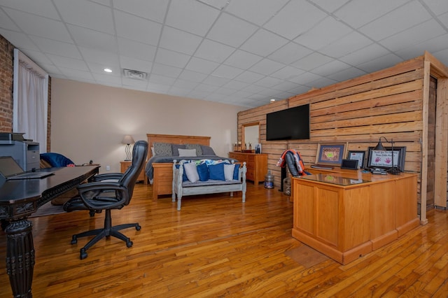 home office with light wood-type flooring, a paneled ceiling, and wooden walls