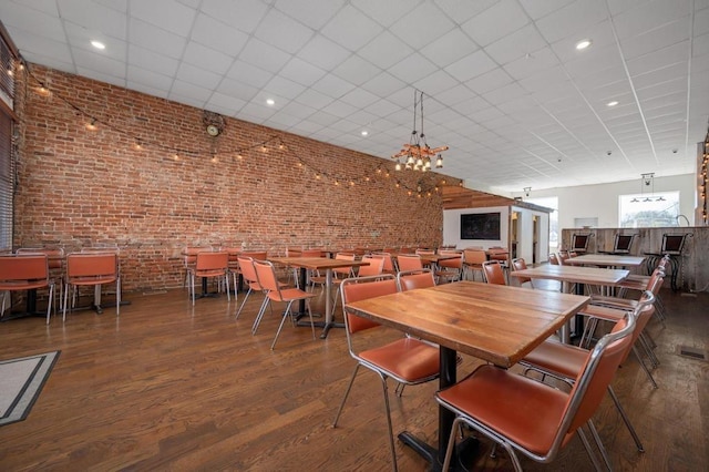 dining area with dark wood-type flooring, brick wall, and a notable chandelier