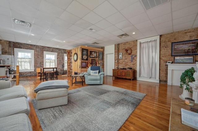 living room with brick wall, a drop ceiling, and hardwood / wood-style floors