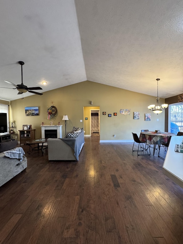 living room featuring vaulted ceiling, dark hardwood / wood-style flooring, ceiling fan with notable chandelier, and a textured ceiling