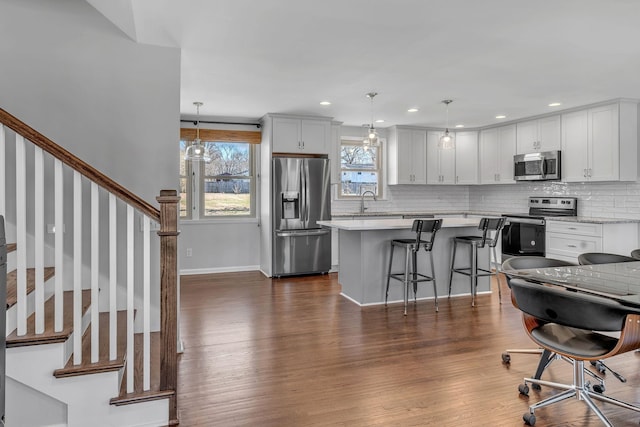 kitchen featuring decorative light fixtures, a kitchen island, a breakfast bar, stainless steel appliances, and white cabinets