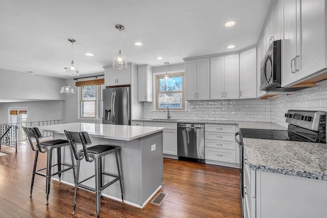 kitchen featuring stainless steel appliances, white cabinetry, hanging light fixtures, and a center island