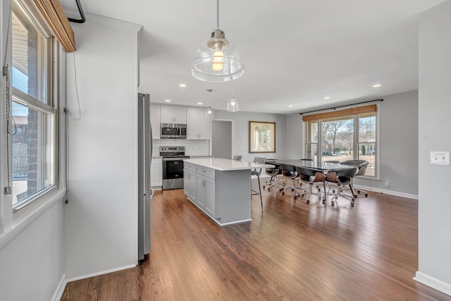 kitchen with decorative light fixtures, a center island, decorative backsplash, white cabinetry, and appliances with stainless steel finishes