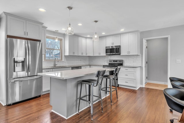 kitchen with appliances with stainless steel finishes, dark hardwood / wood-style floors, decorative light fixtures, a kitchen island, and a breakfast bar