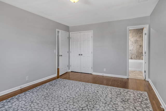 unfurnished bedroom with ensuite bathroom, wood-type flooring, and a closet