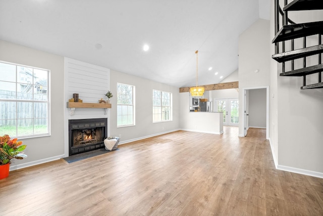 unfurnished living room featuring light wood-type flooring, a notable chandelier, and high vaulted ceiling