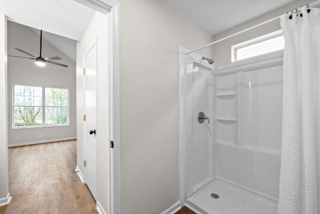 bathroom featuring hardwood / wood-style floors, ceiling fan, lofted ceiling, walk in shower, and a textured ceiling