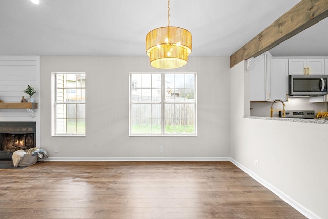 interior space featuring a fireplace, beamed ceiling, a notable chandelier, and hardwood / wood-style floors